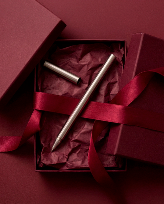 Design kuglepen i stål fra A Pen Company præsenteret som gave i æske med bordeaux silkepapir og bånd.