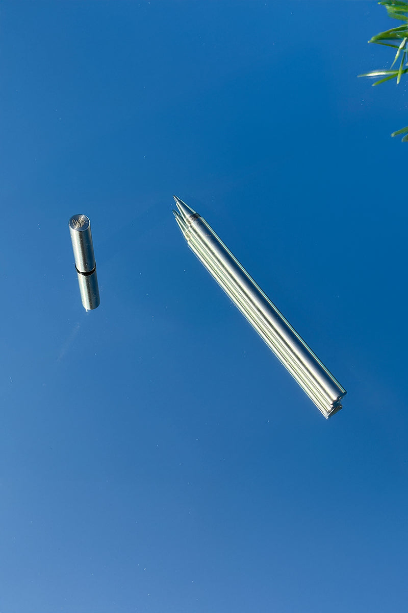 Stålkuglepen fra A Pen Company fotograferet på spejl under blå himmel – minimalistisk designpen i stål.